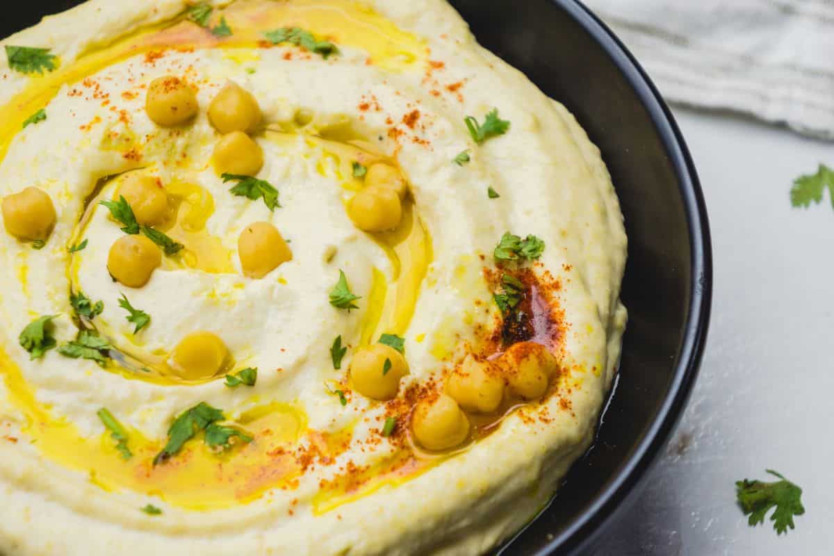 Creamy hummus topped with chickpeas, olive oil, paprika, and cilantro in a black bowl.