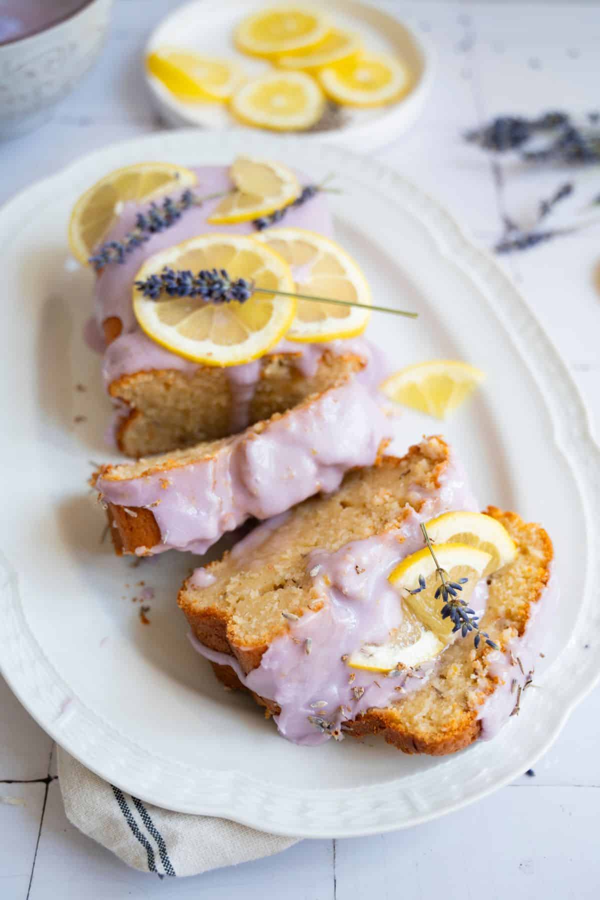 Delicious lemon bundt cake drizzled with lemon glaze, topped with lavender sprigs, served on a white dish.