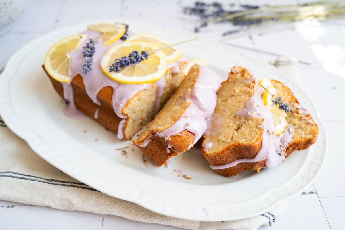 Delicious lemon lavender cake topped with lemon slices and lavender, served on a white plate. Perfect for tea or dessert.