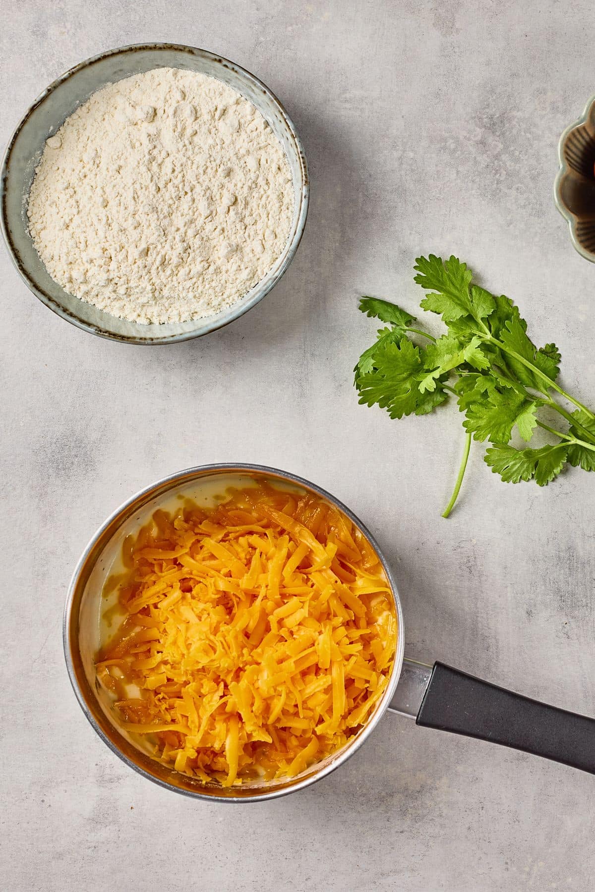 Fresh shredded cheddar cheese, flour, and cilantro for cooking or baking recipes.