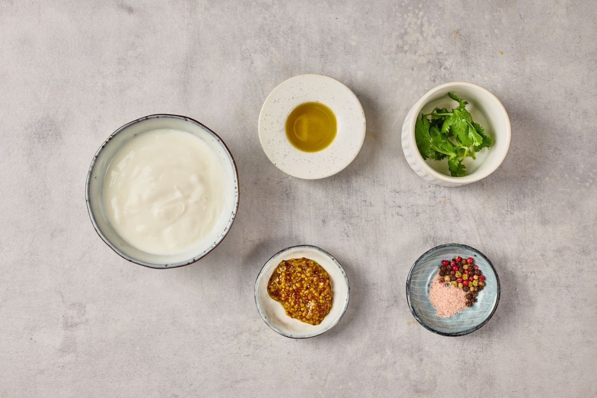 Close-up of yogurt, olive oil, herbs, and spices on a textured gray background.