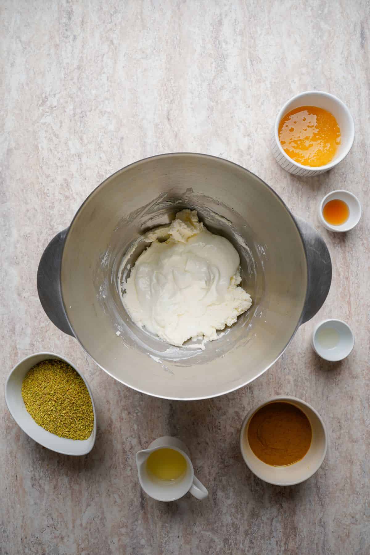 Alt text: Cream cheese and ingredients for a baking recipe, surrounded by small bowls of flavorings.
