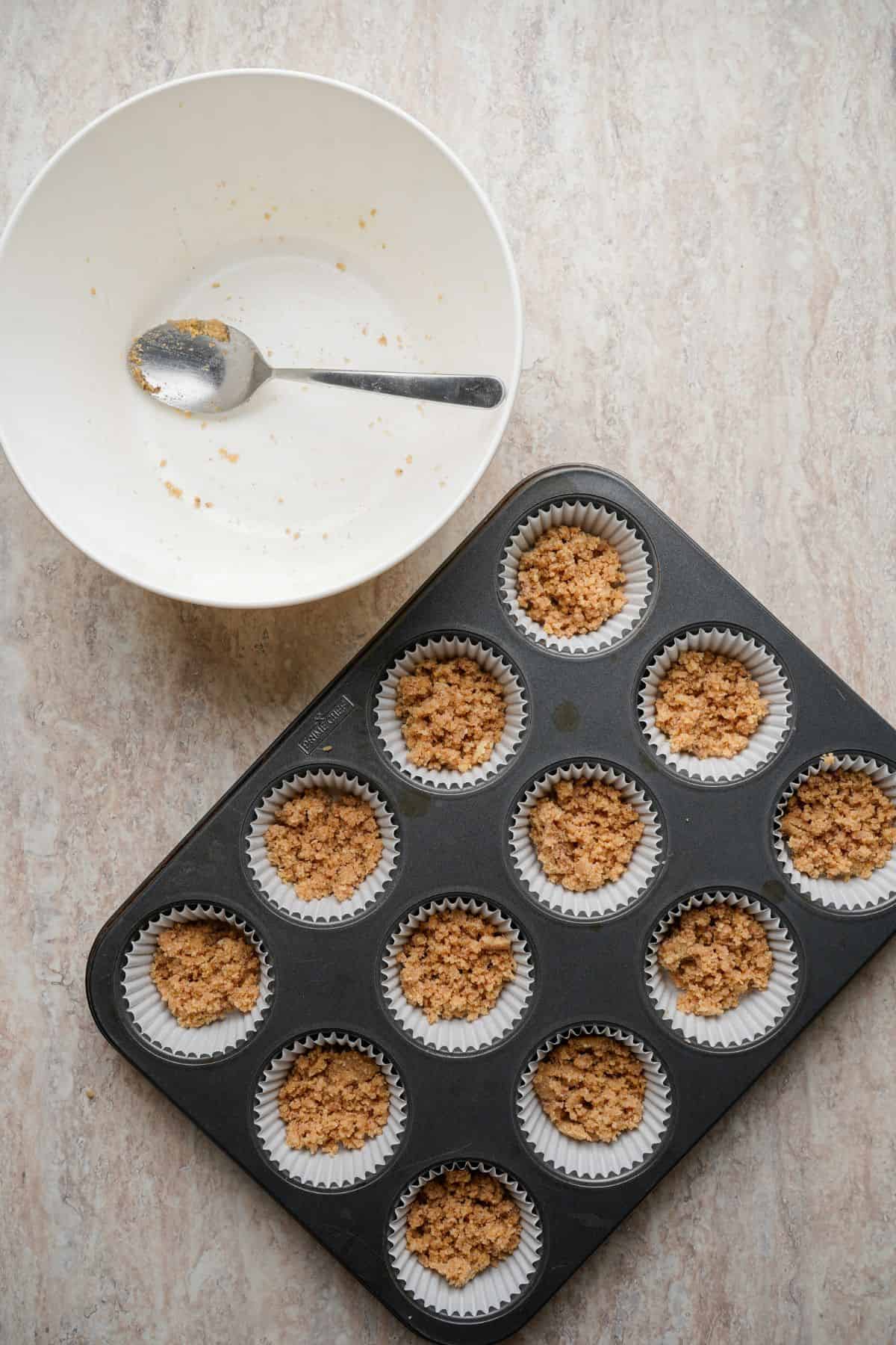 Delicious cookie dough ready for baking in a muffin tin with a mixing bowl nearby.