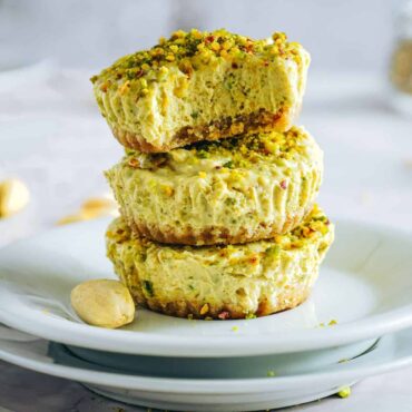 Delicious pistachio cheesecake with chopped nuts on top, served on a white plate. An indulgent dessert option.