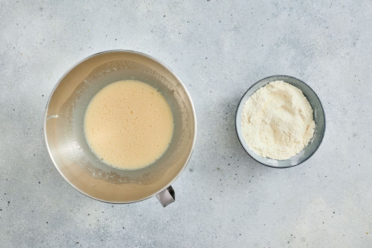 A mixing bowl with batter and a small bowl of flour on a grey surface. Perfect for baking recipes.