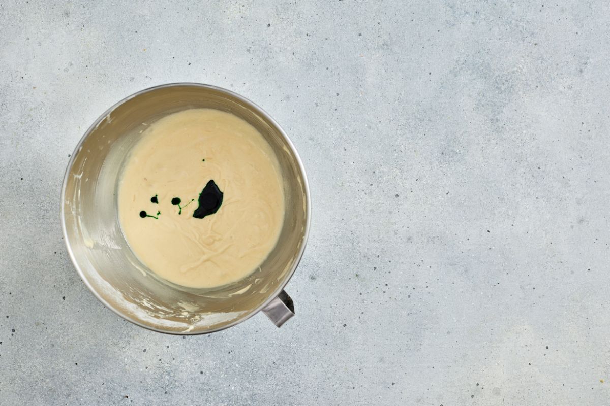 Batter with black ink drops in a stainless steel mixing bowl for cooking or baking.