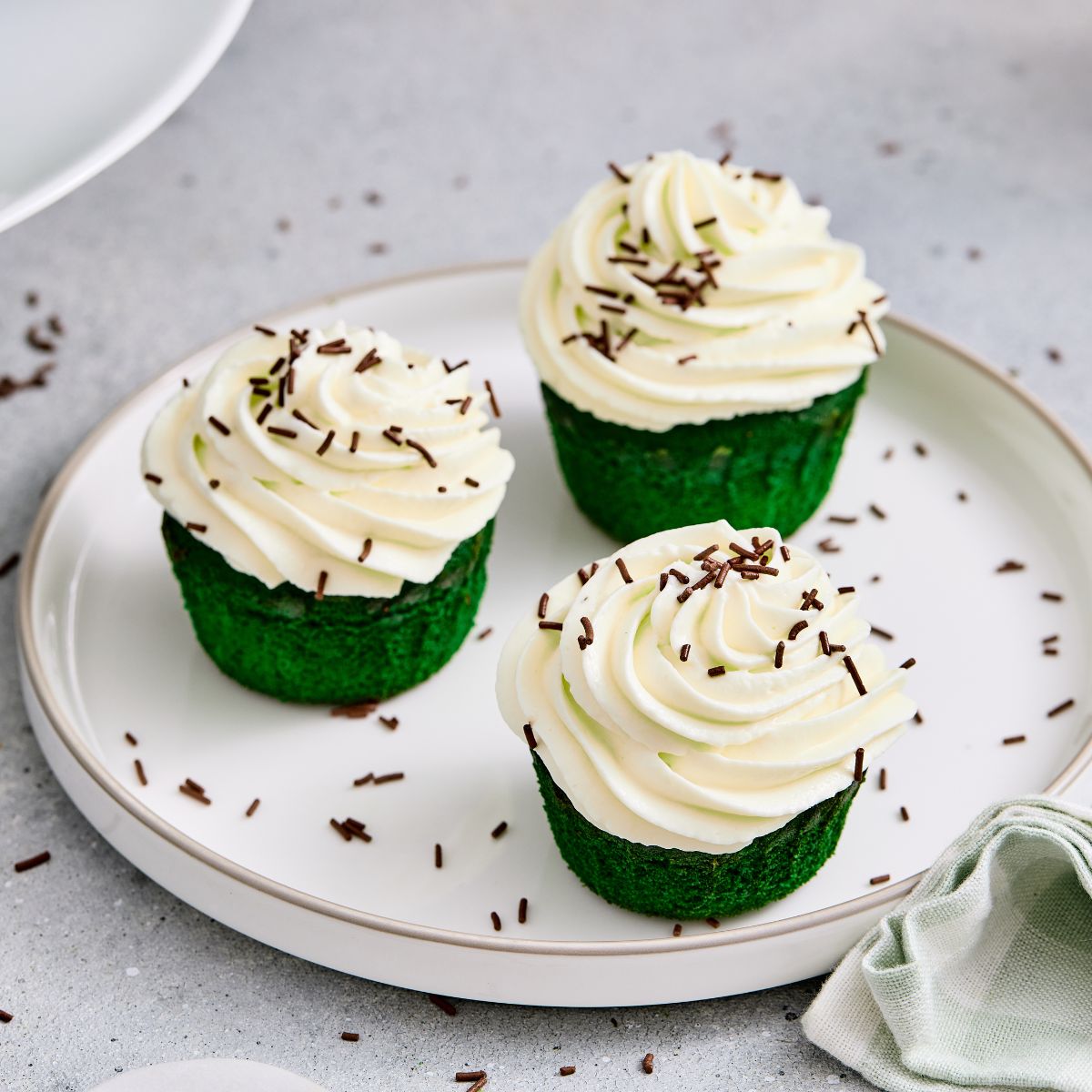 Delicious cupcakes topped with white frosting and chocolate sprinkles, served on a white plate.