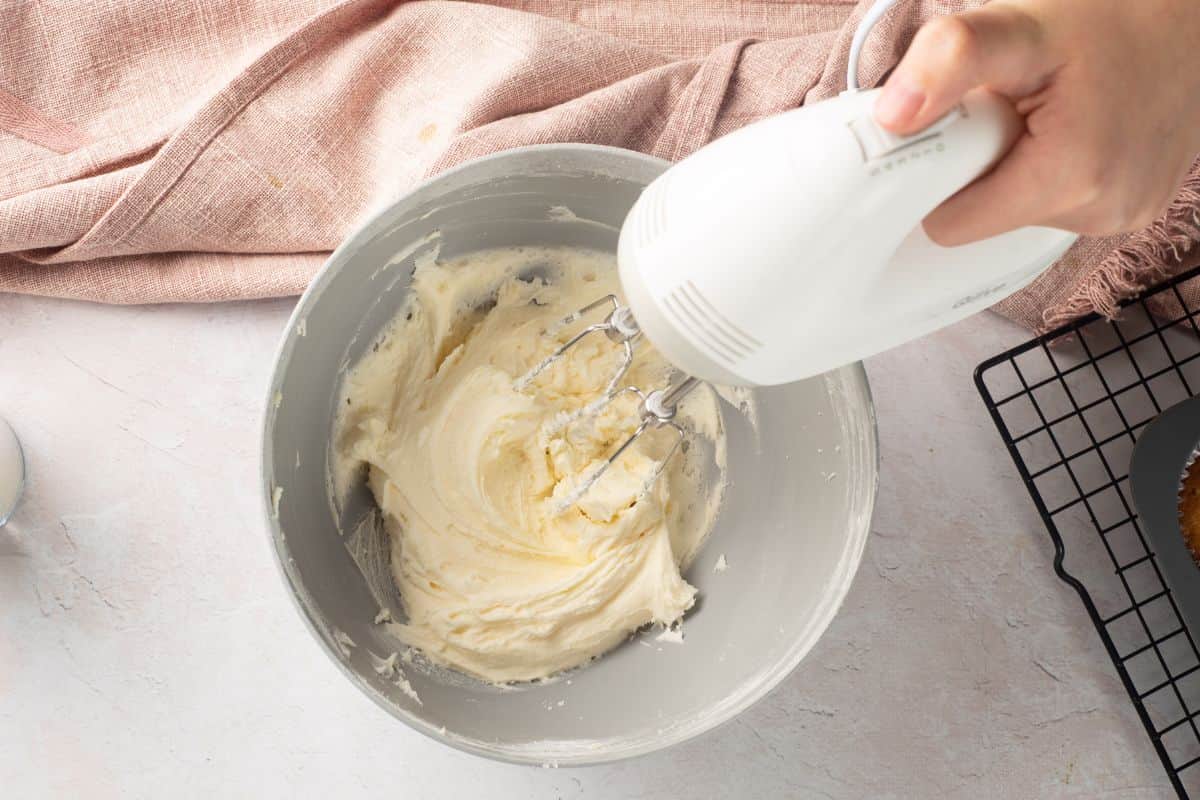 Hand mixer blending creamy butter and sugar for frosting.