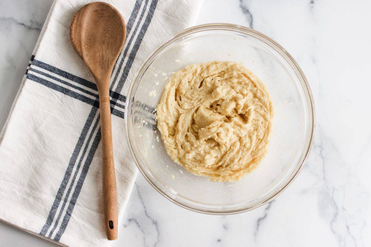 Cookie batter mixture in a large bowl with a spatula resting inside, set on a cloth-covered surface.
