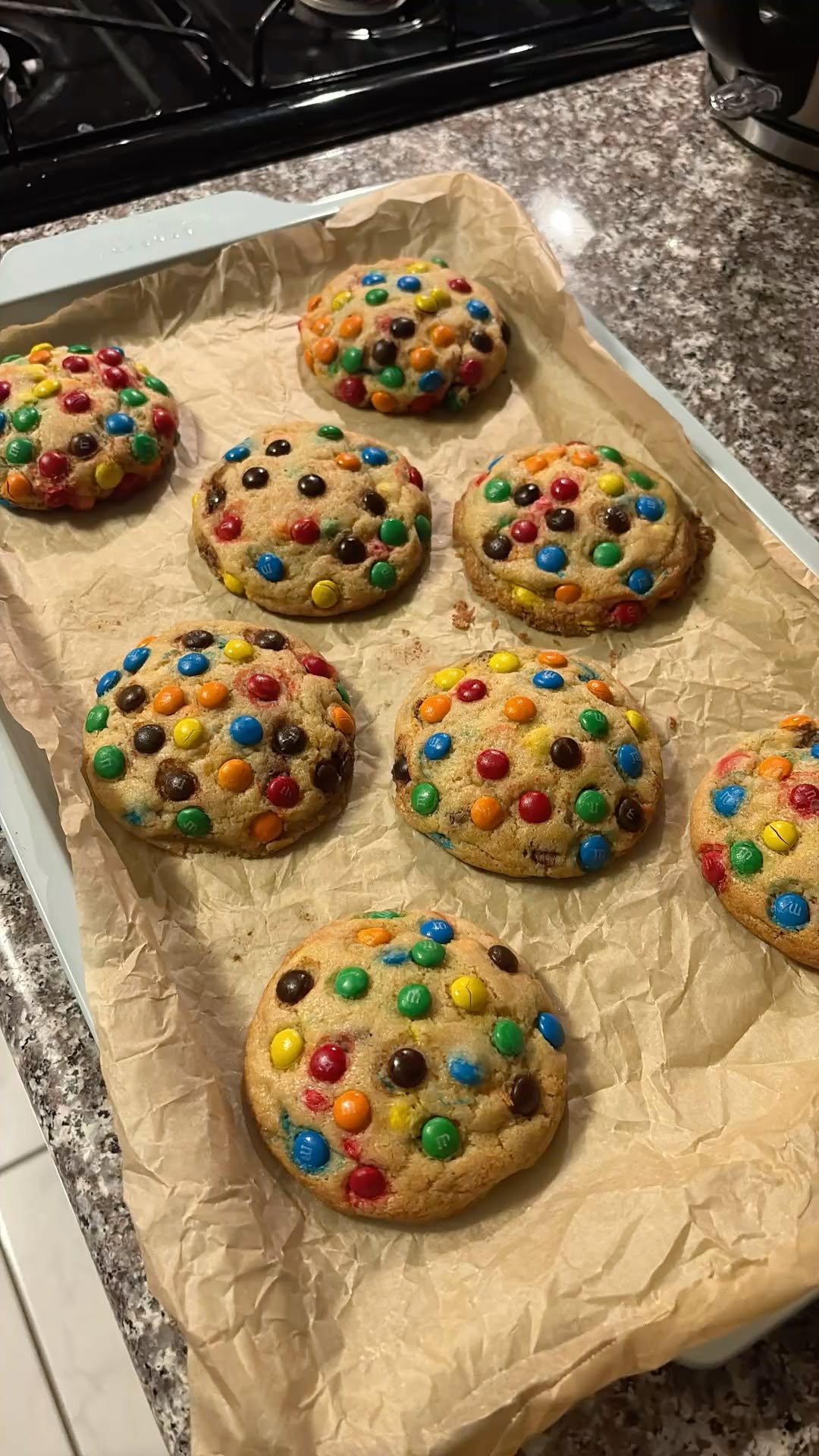 A baking sheet lined with parchment paper holds several freshly baked cookies studded with colorful candy pieces.