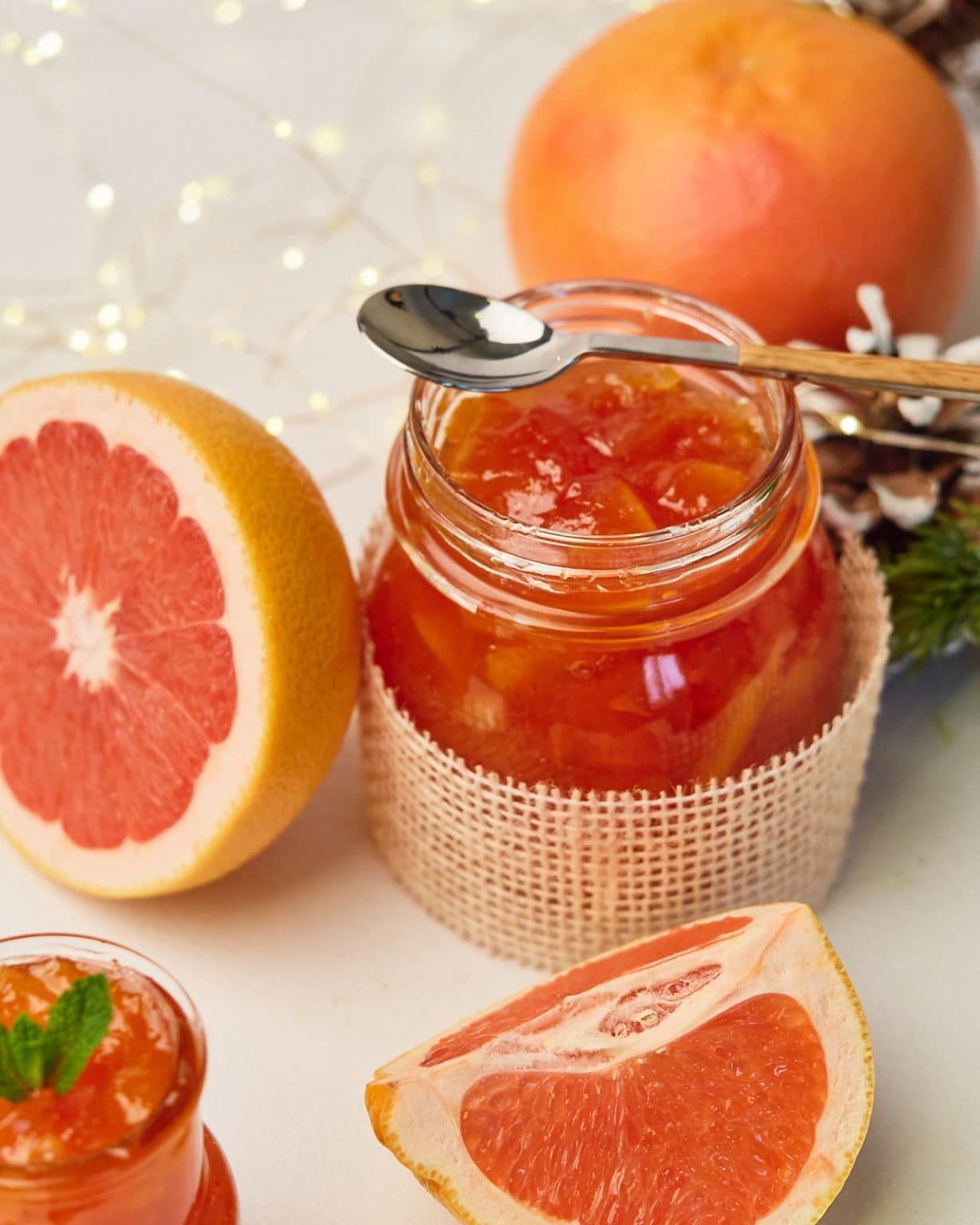 Jar of orange marmalade with spoon, surrounded by fresh grapefruit halves and wedges