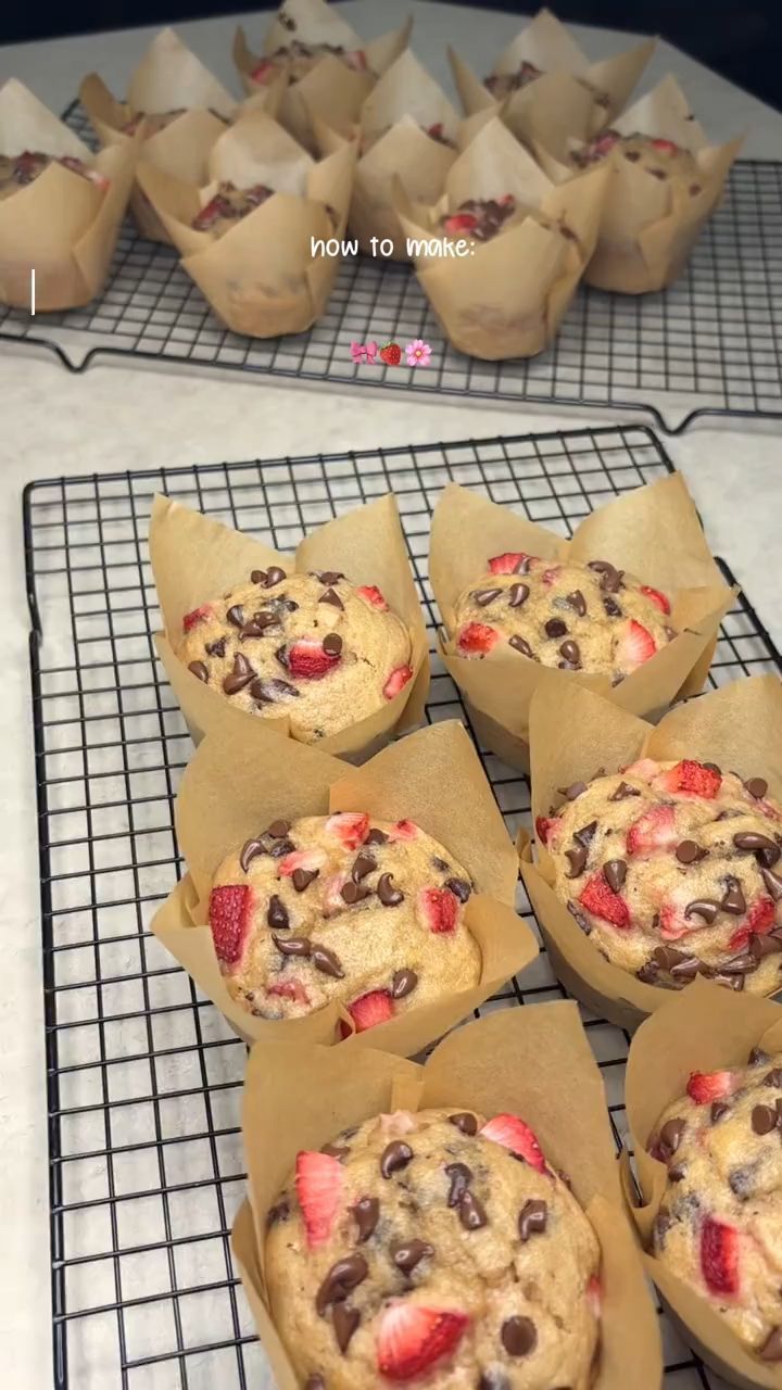 Several strawberry chocolate chip muffins in brown tulip-style liners, cooling on a wire rack.