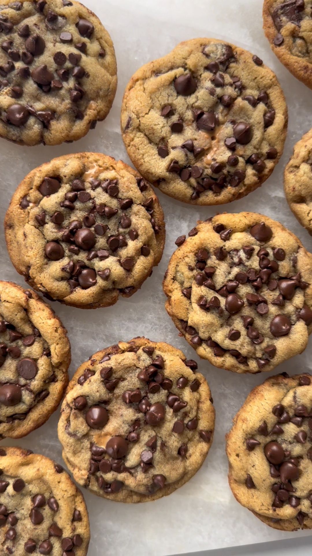 Several round, golden-brown chocolate chip cookies with melted chocolate chips visible on top, arranged on a light surface.
