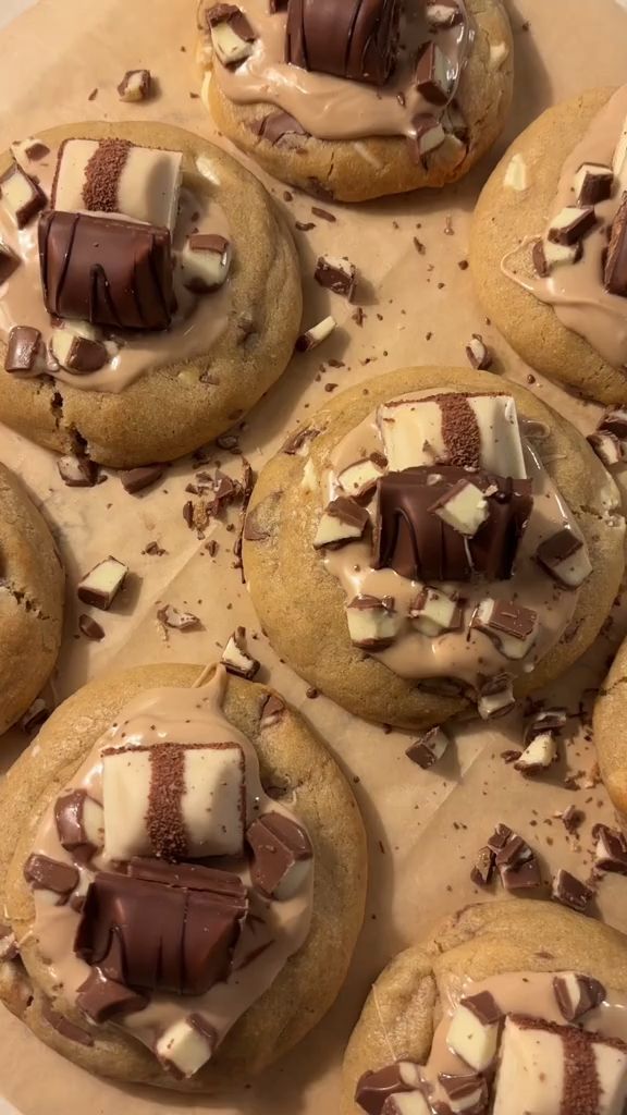 Close-up of several chunky chocolate chip cookies on parchment paper, topped with melted chocolate and chocolate bar pieces.