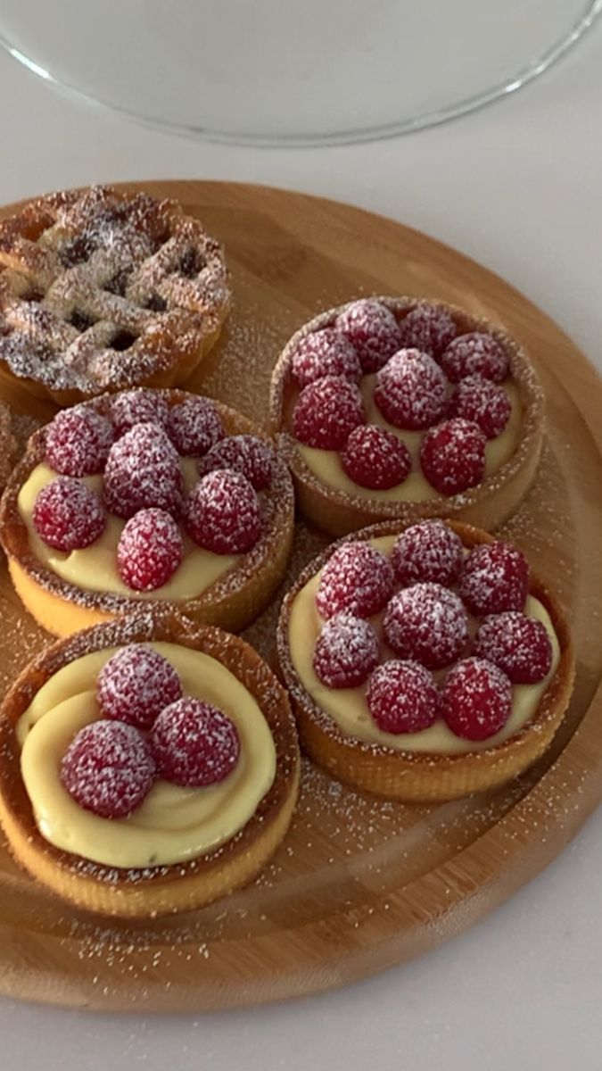 Small round tarts with raspberries and powdered sugar on a wooden tray.