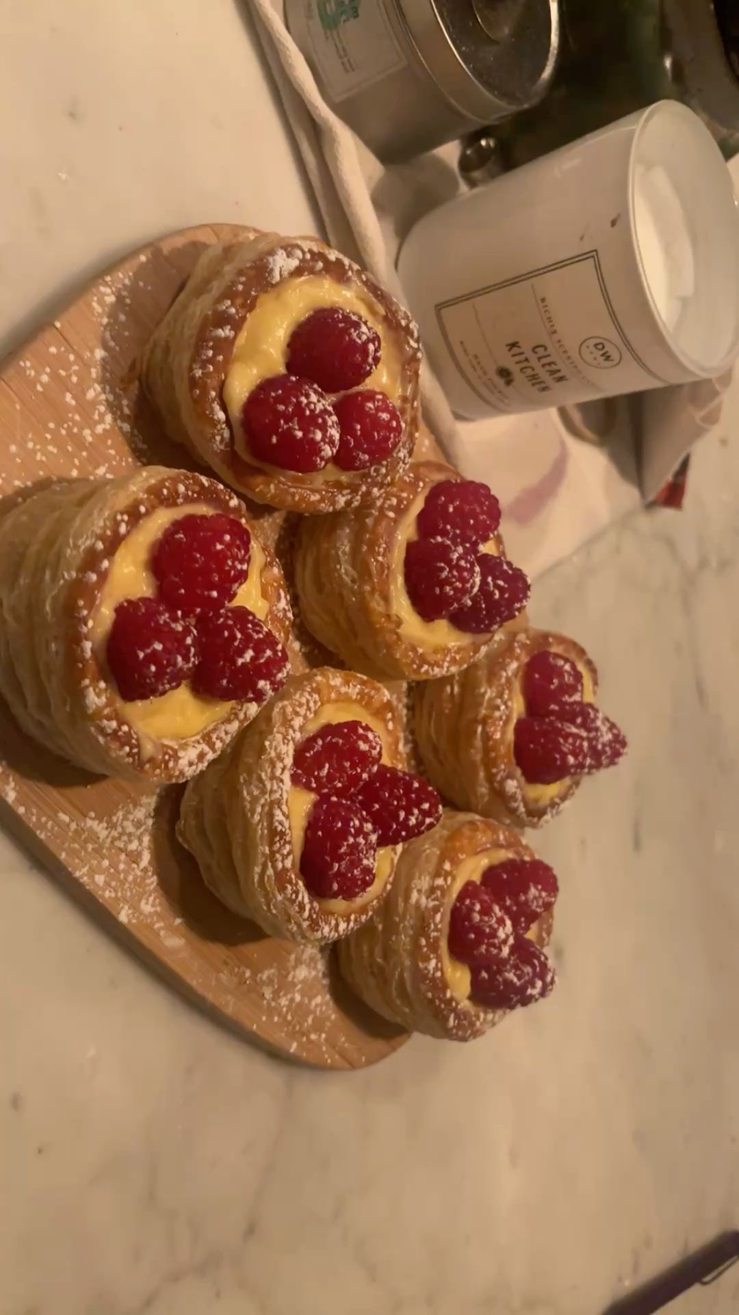 Several raspberry and cream-filled pastries dusted with powdered sugar, arranged on a small wooden tray.