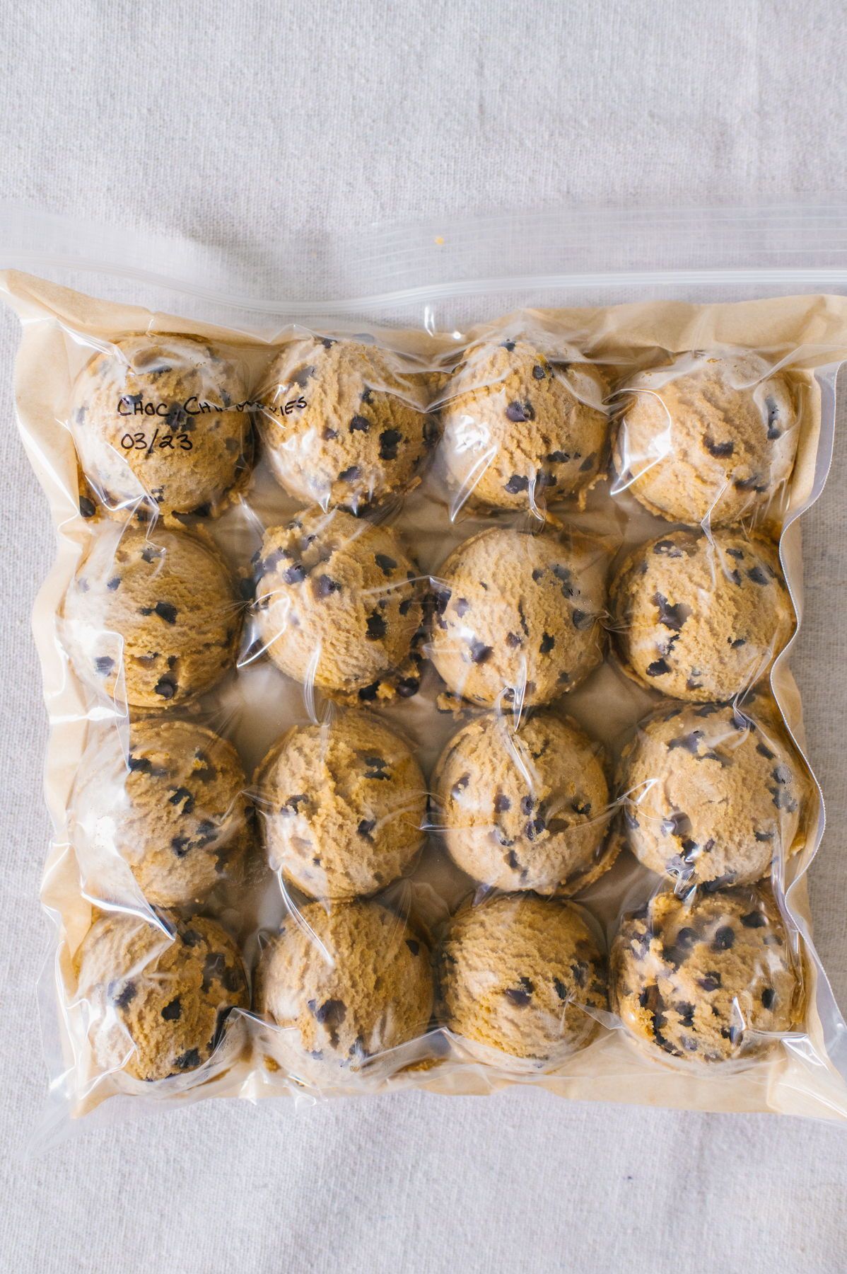 Scoops of chocolate chip cookie dough arranged on parchment paper inside a clear freezer bag.