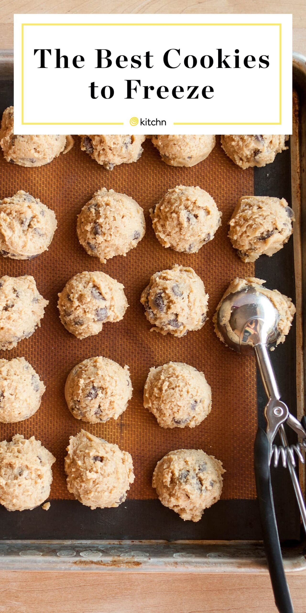 Scoops of chocolate chip cookie dough arranged on a baking sheet lined with a silicone mat, with a cookie scoop next to them.