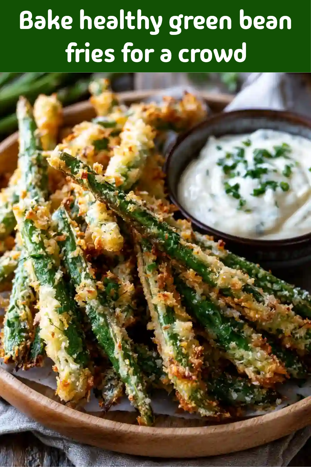 Close-up of baked green bean "fries" on a wooden platter with a small bowl of white dipping sauce topped with chives.