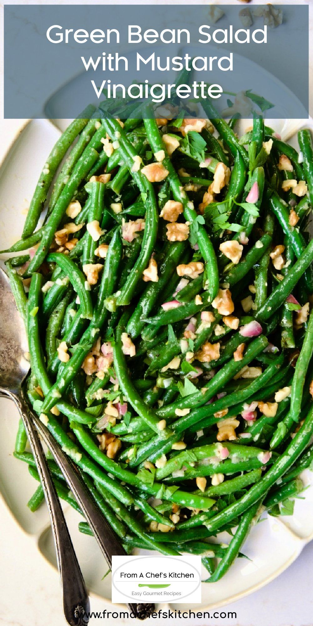 Green bean salad with chopped walnuts, red onion, and parsley on a white platter with serving spoons