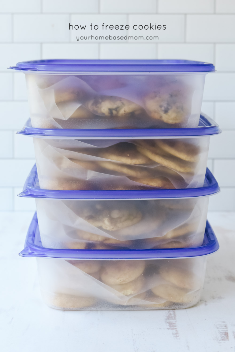 Stack of four clear rectangular plastic containers with purple lids, each holding cookies separated by parchment paper.