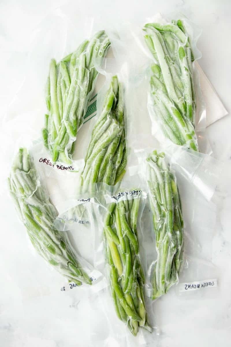 Several vacuum-sealed bags of frozen green beans arranged on a light surface.