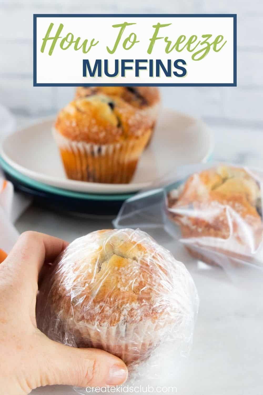A hand holding a muffin wrapped in plastic, with more muffins on plates and in freezer bags in the background.