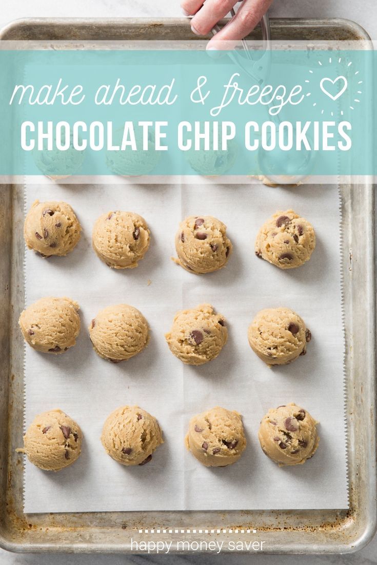 Scoops of chocolate chip cookie dough lined up on parchment paper on a baking sheet, ready for freezing.