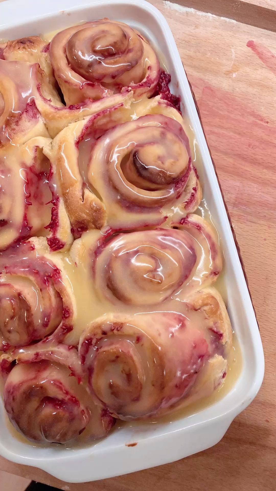 A rectangular baking dish filled with several baked raspberry lemon rolls, generously covered in a white glaze.