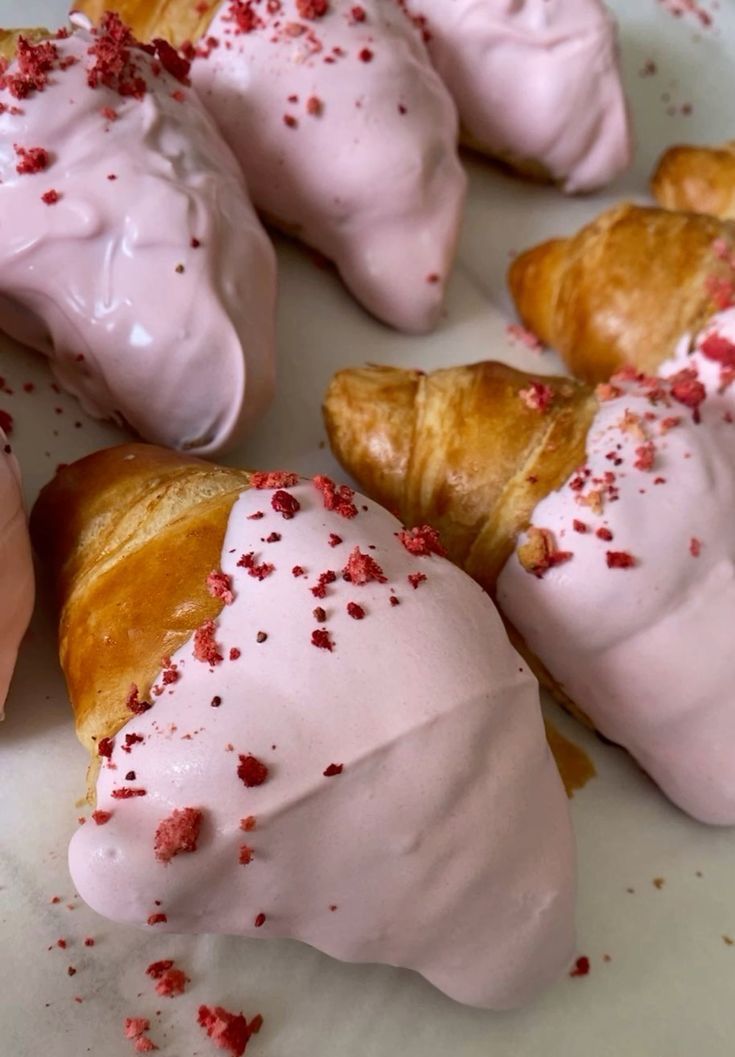 Several golden-brown croissants, some partially dipped in a light pink glaze and sprinkled with red freeze-dried fruit bits.