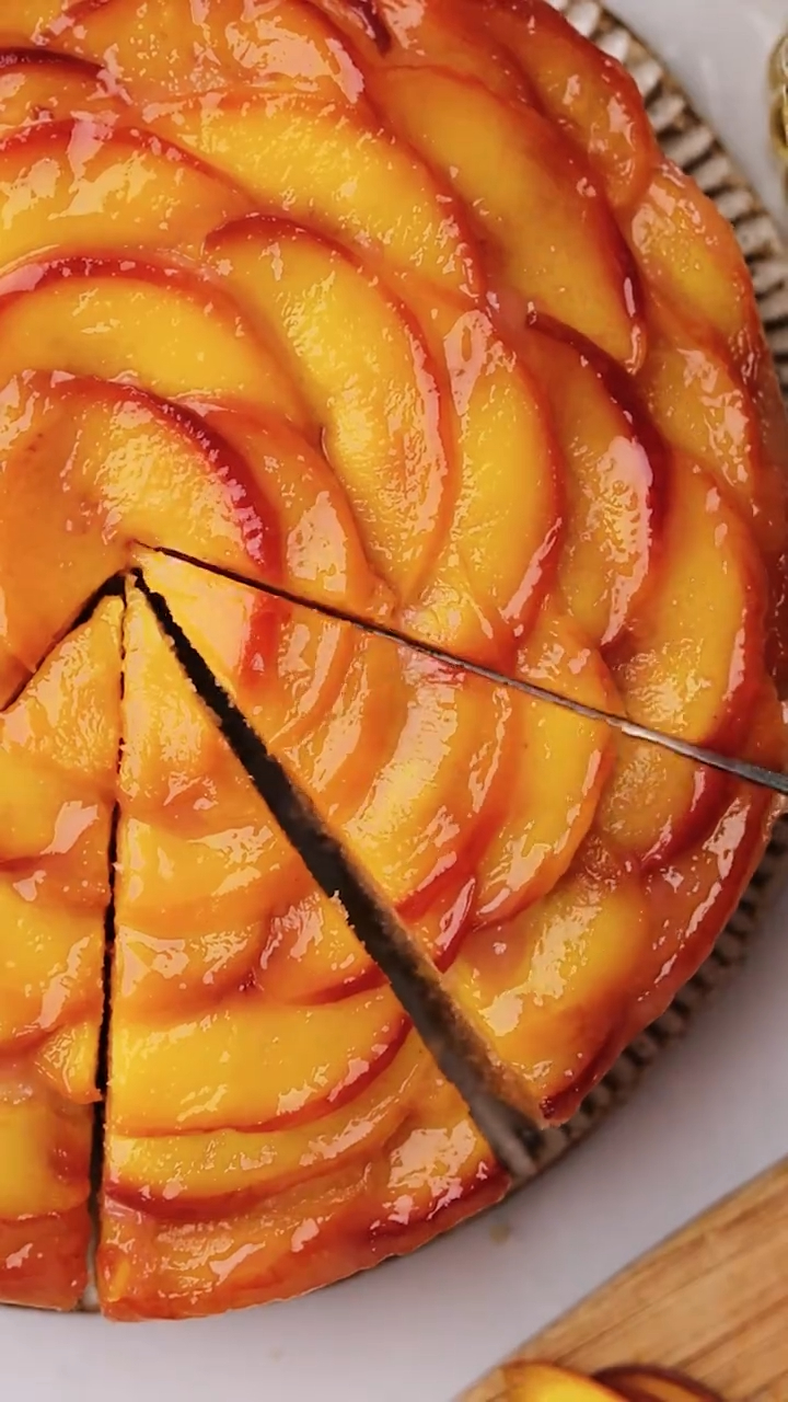 A round, golden-brown peach preserve cake with a glossy topping of sliced peaches arranged in concentric circles.