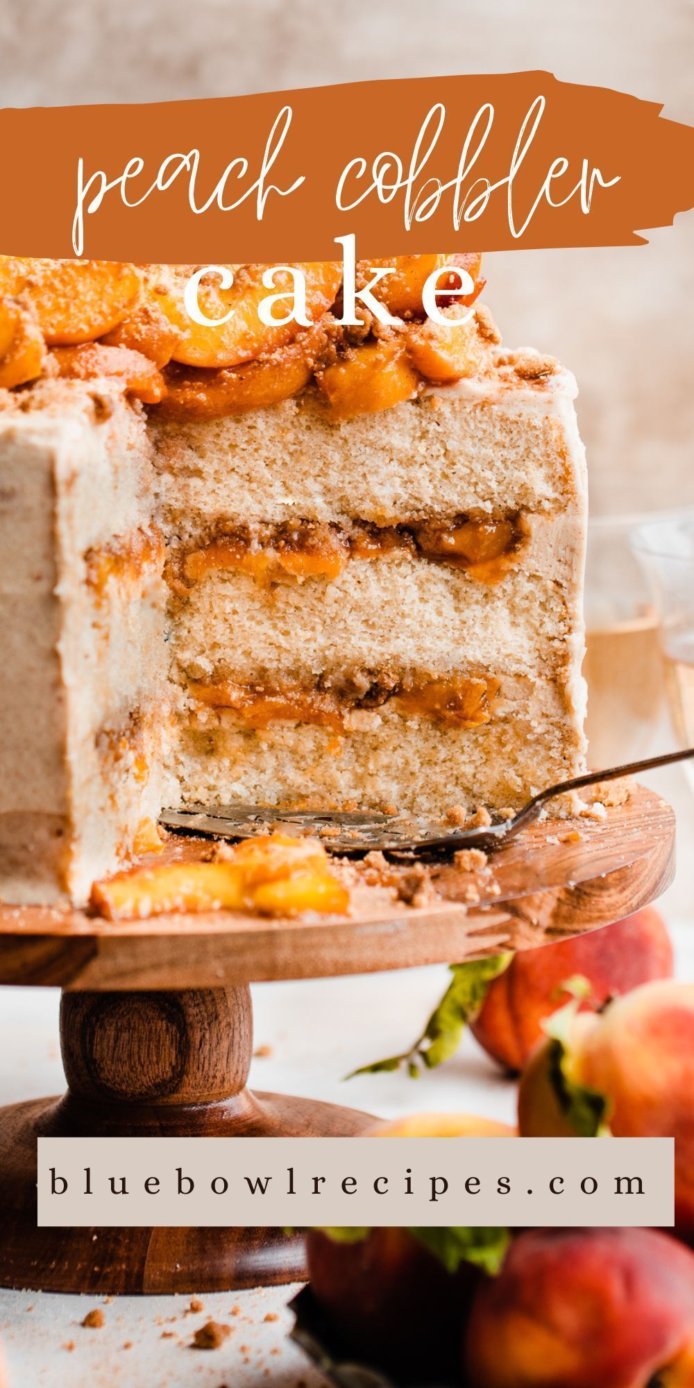 Slice removed from a peach cobbler layer cake, revealing peach filling between cake layers, with fresh peaches arranged on…