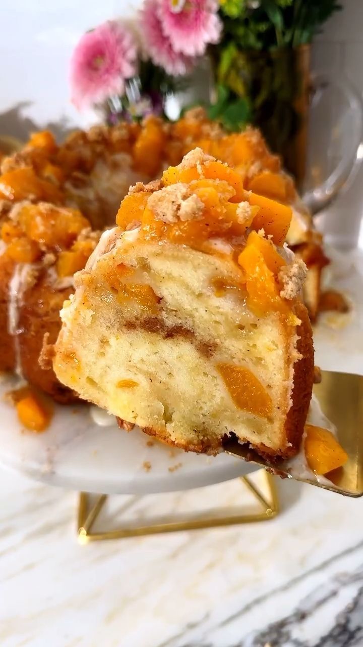 A slice of peach pound cake with diced peaches and streusel on top, being lifted from a larger cake.