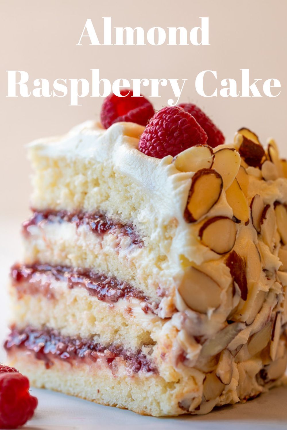 Slice of triple-layer almond cake with white frosting, raspberry jam filling, whole raspberries, and sliced almonds.