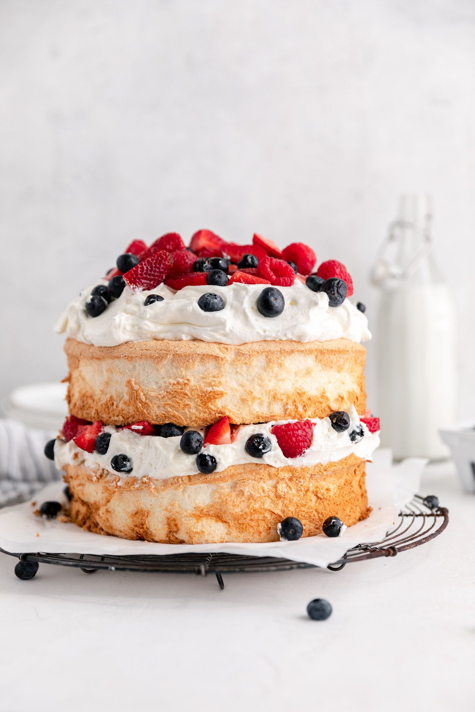 A two-layer angel food cake filled and topped with whipped cream, strawberries, raspberries, and blueberries.