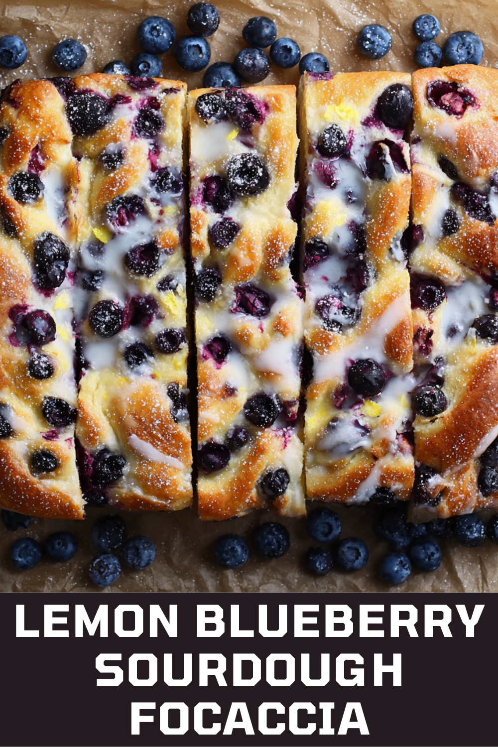 Slices of sourdough focaccia with blueberries, lemon zest, and white icing or glaze on a piece of parchment paper, with…