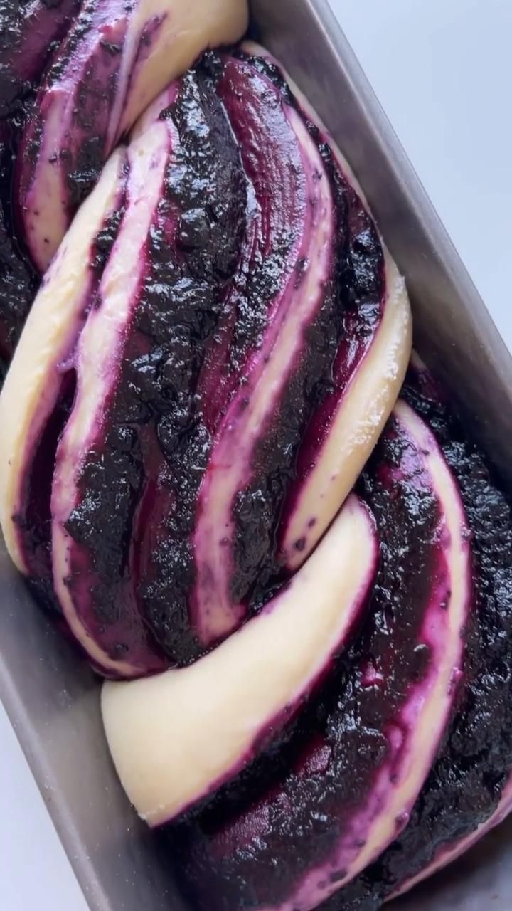 Close up of a blueberry swirled sourdough babka dough in a loaf pan, showing distinct layers of purple and beige dough.