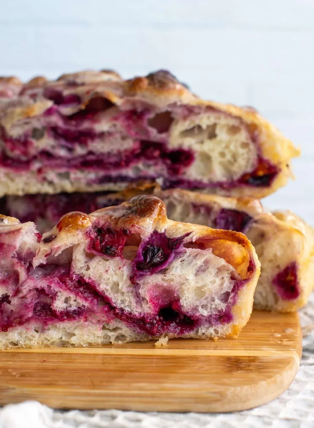 Close-up of three pieces of focaccia bread with purple-red berry filling, stacked on a wooden board.