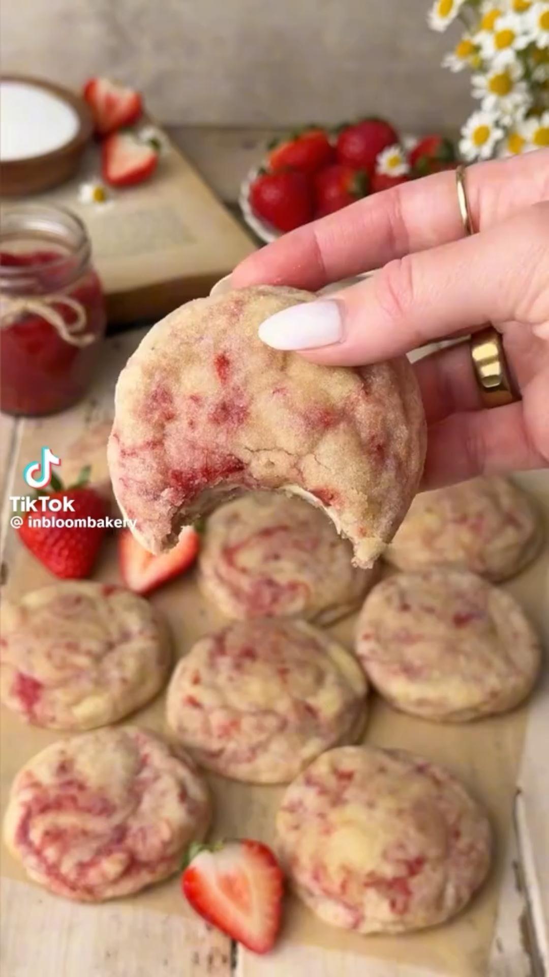 A hand holds up a strawberry swirl cookie with a bite taken out, revealing its soft interior.