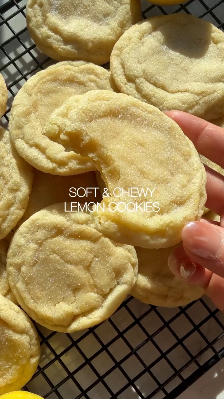 Lemon cookies with a sugary coating on a cooling rack, with a hand picking one up