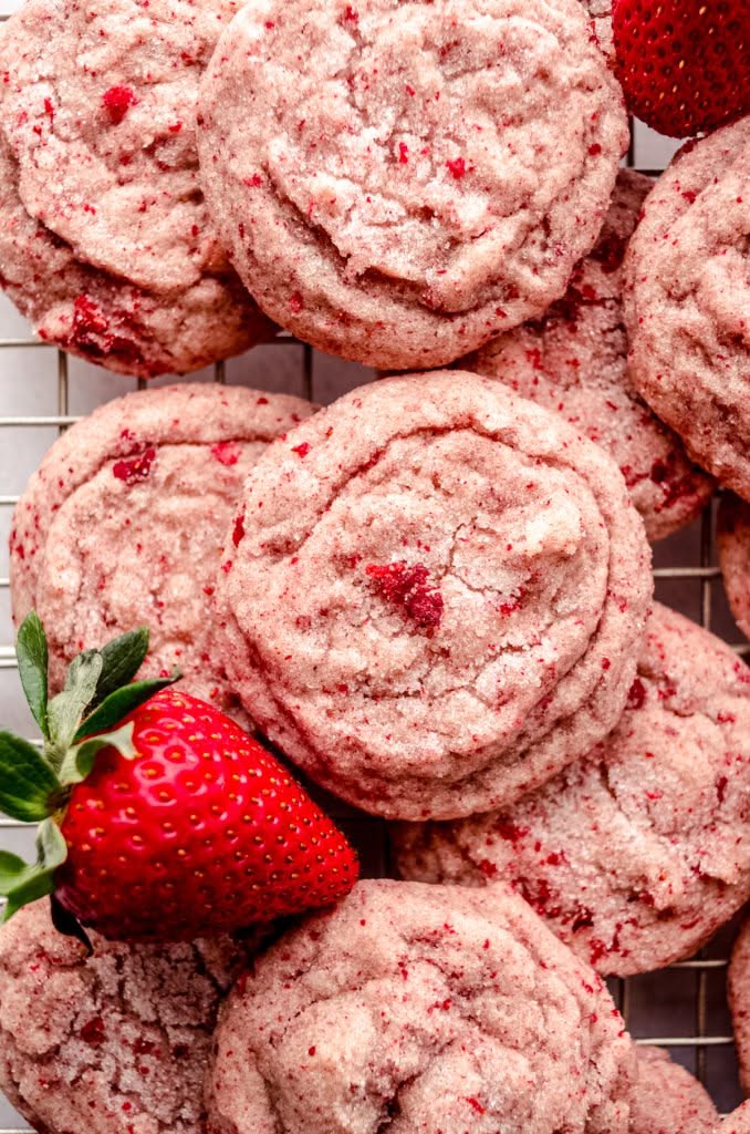 Several pink cookies with red flecks, one whole strawberry with a green stem and leaves