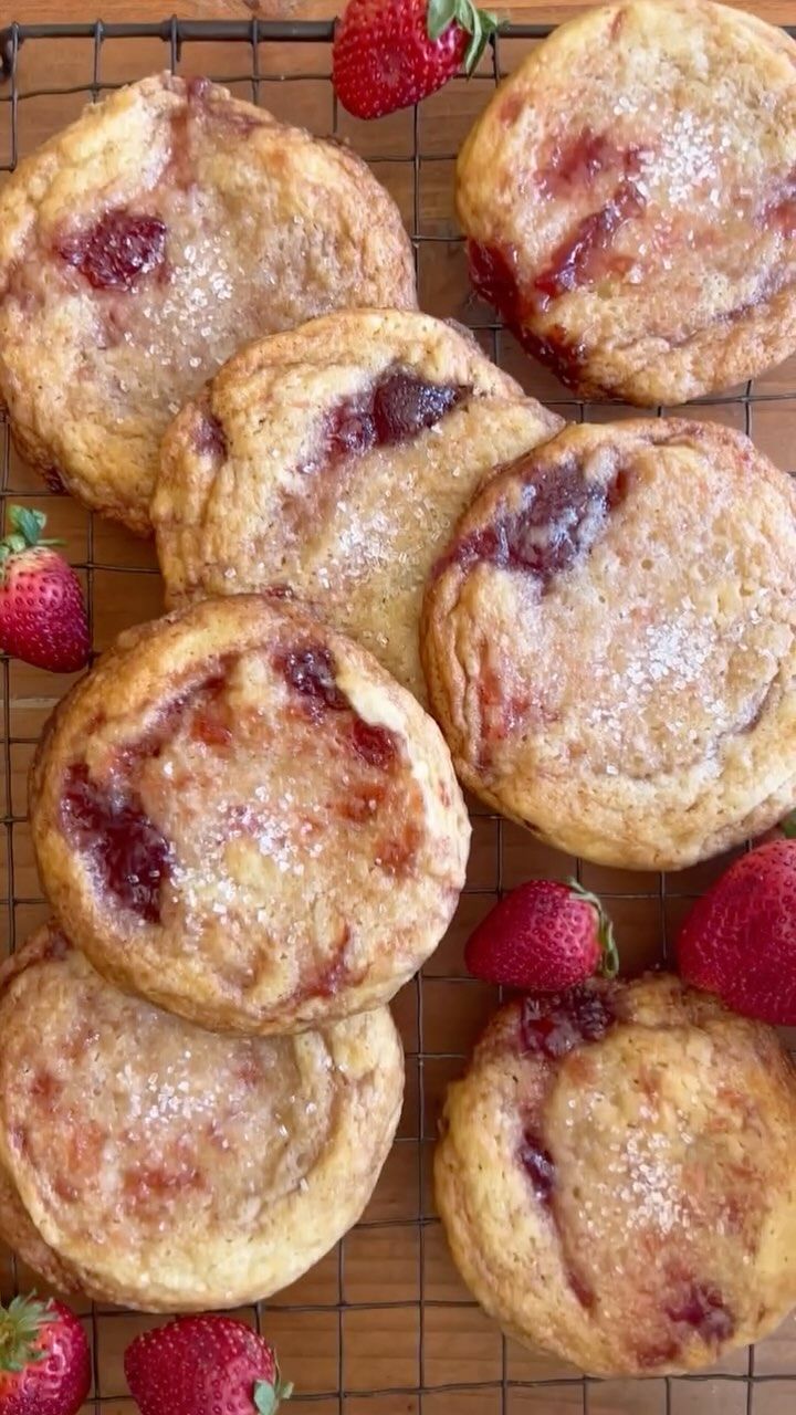 Several round, flat sugar cookies with visible strawberry jam swirls and a light sprinkle of sugar on a wire cooling rack…