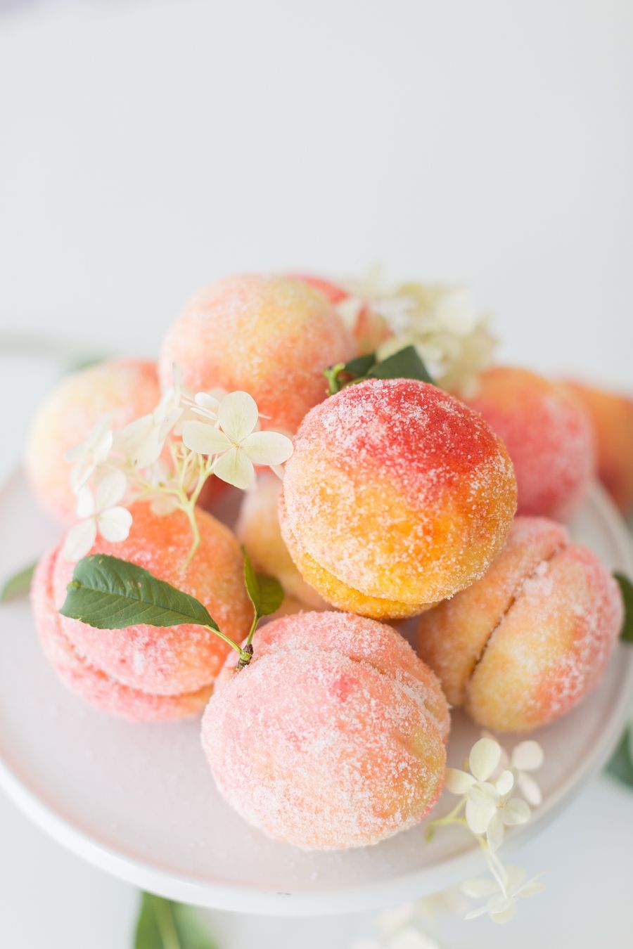 Several Italian peach cookies on a white serving plate, garnished with small white flowers and green leaves.