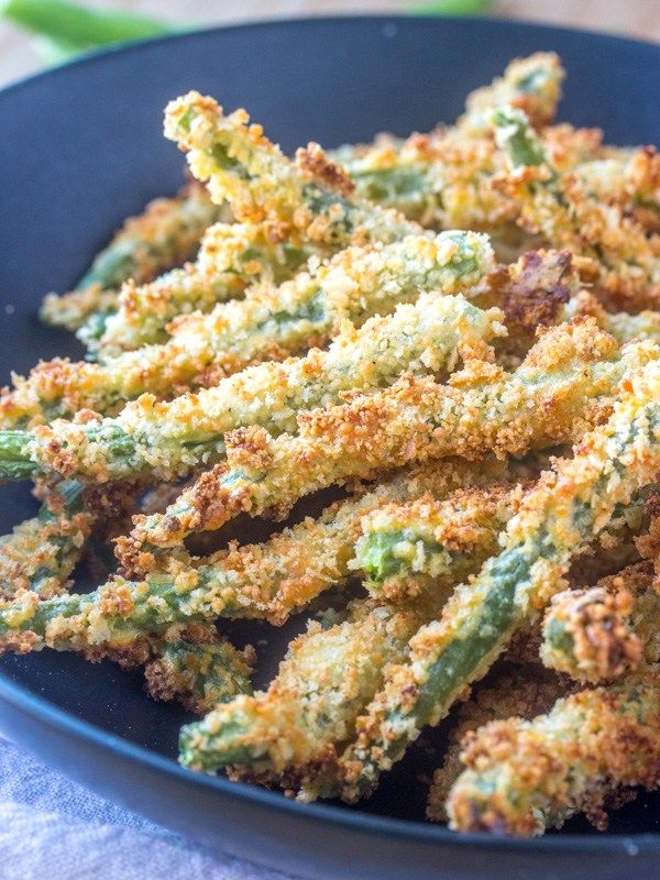 Close-up of baked green bean fries, coated in a crispy, golden-brown breading, served in a black bowl.