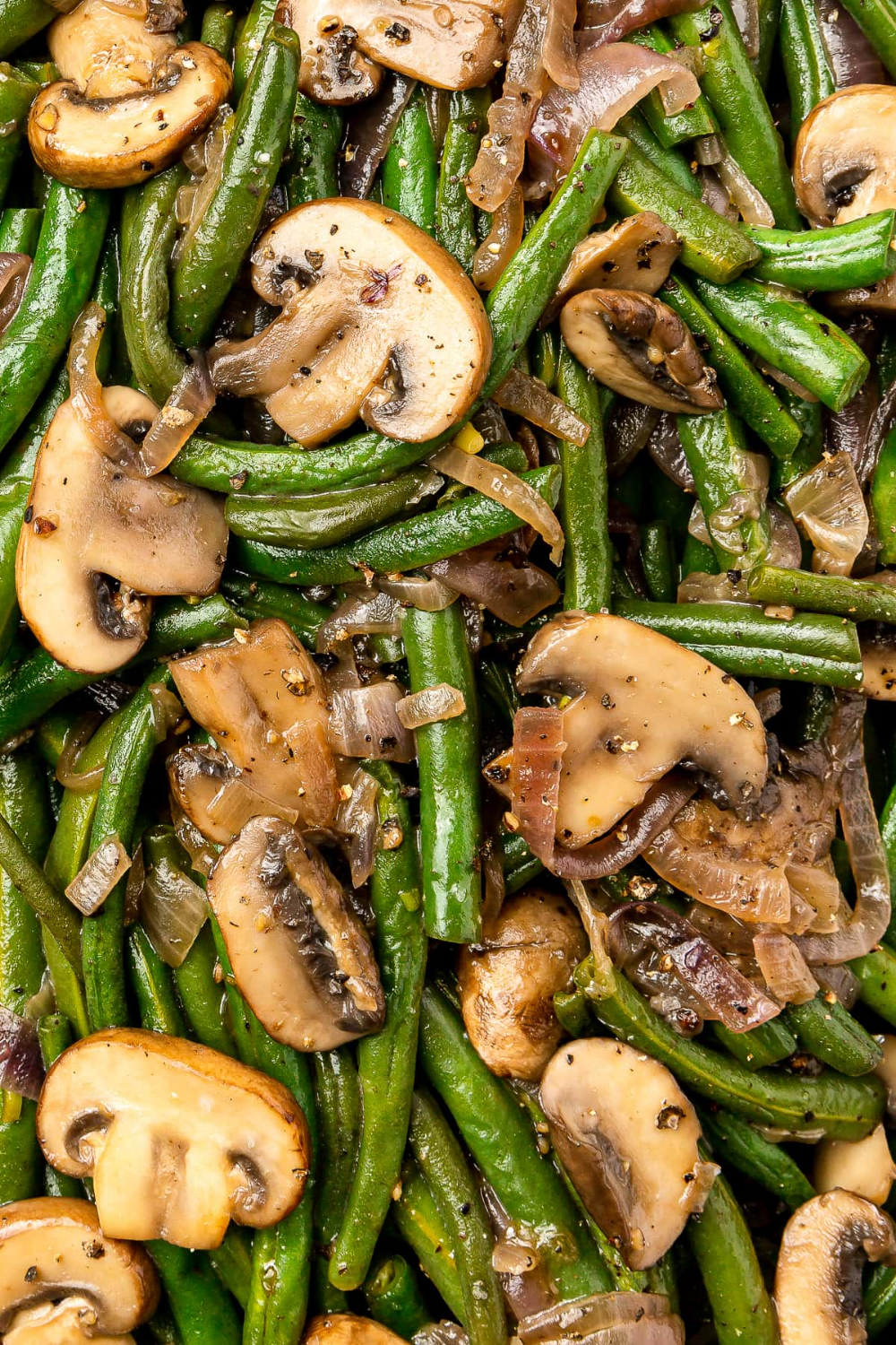 Close-up of baked green beans and sliced mushrooms with sautéed onions seasoned with black pepper
