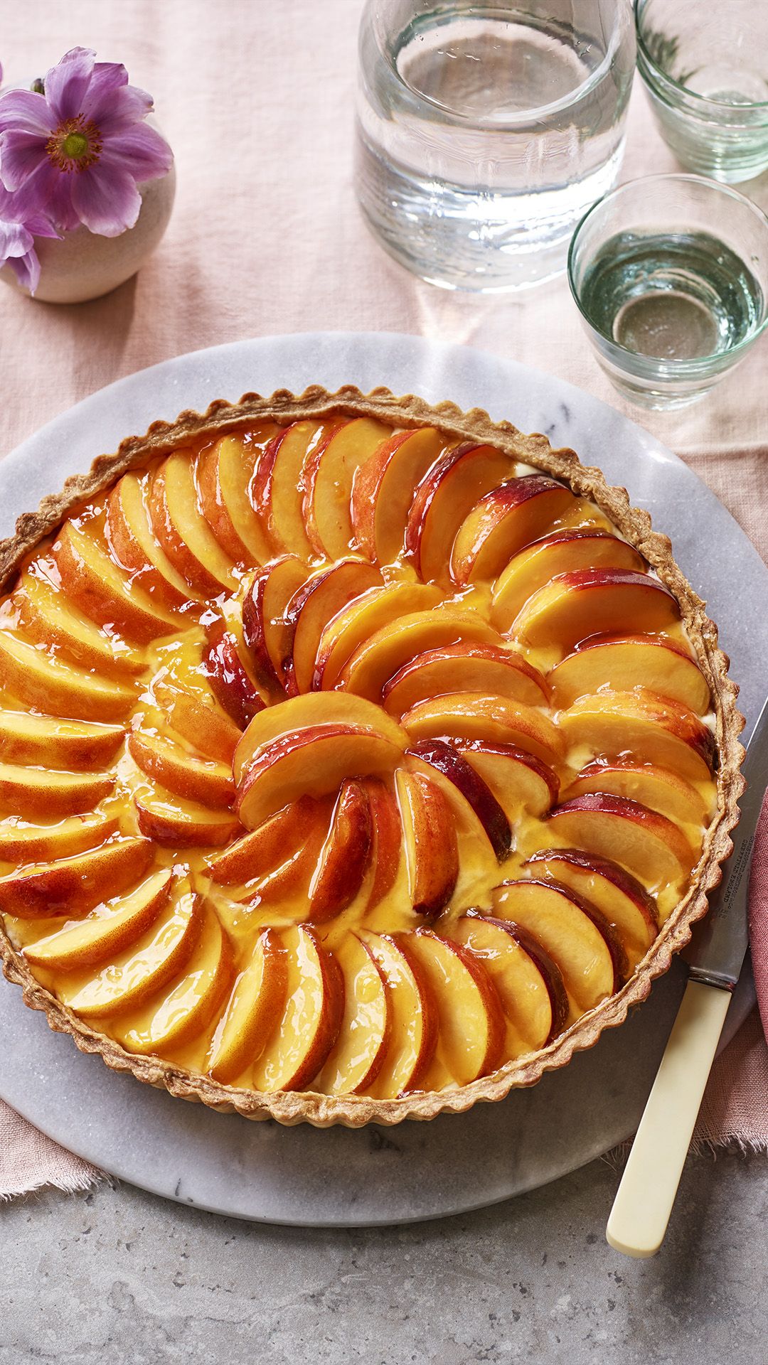Round peach tart with sliced peaches arranged in concentric circles over a creamy filling inside a crimped pastry crust.