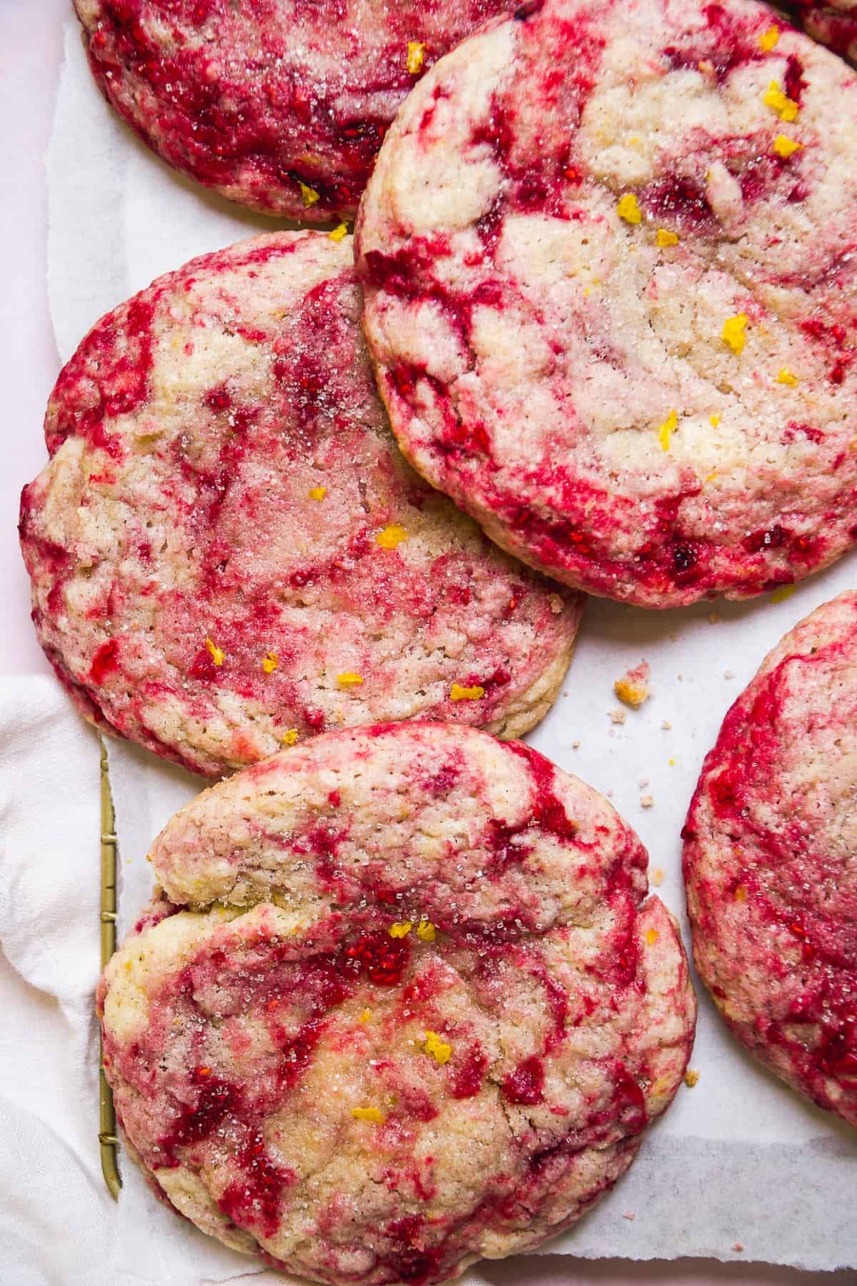 Close up of several lemon raspberry swirled cookies on a white surface, speckled with yellow lemon zest.