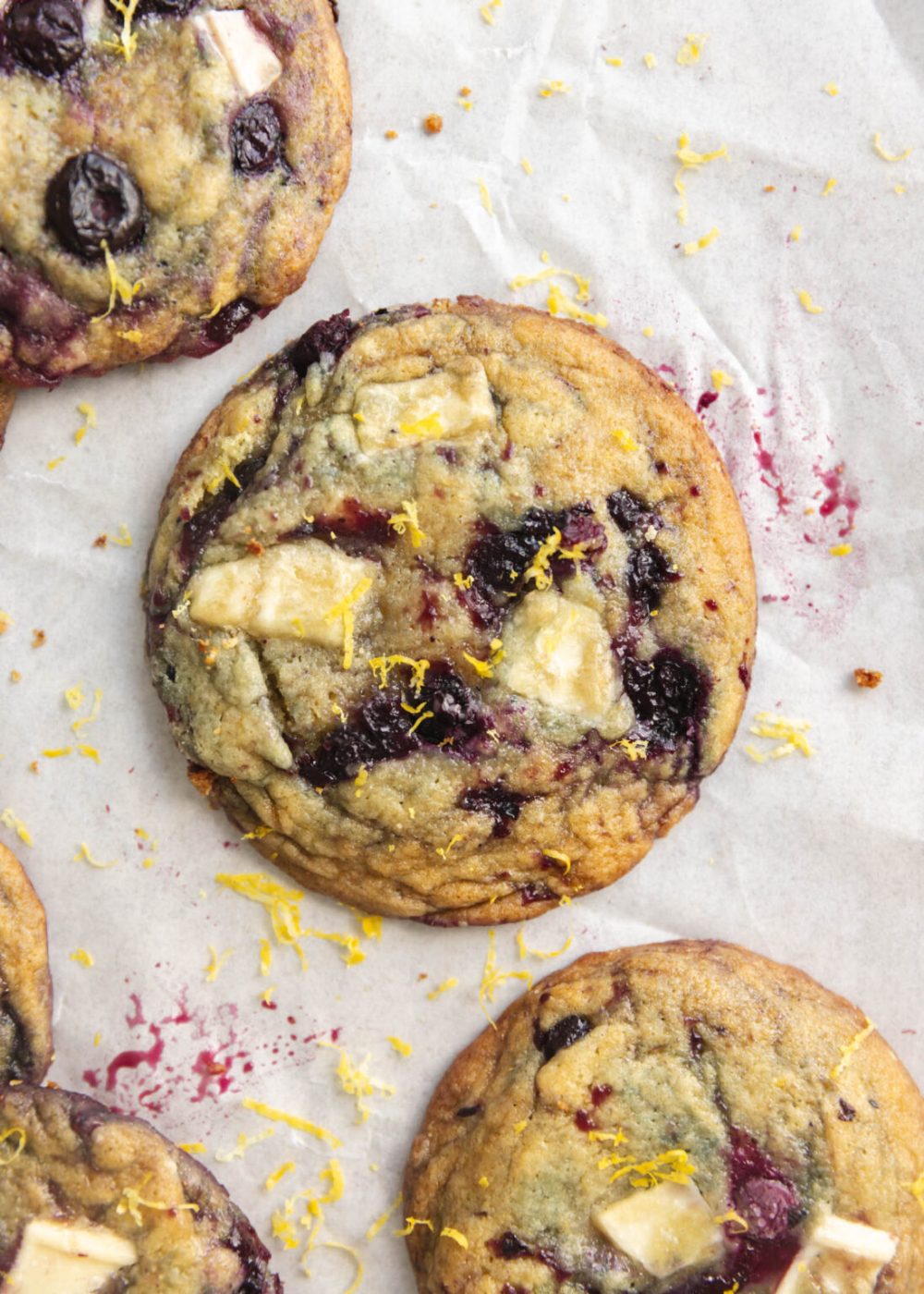 Close up of several lemon blueberry cookies with white chocolate pieces, garnished with lemon zest.