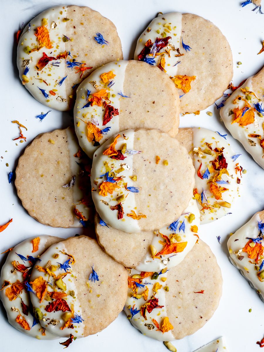 Close-up of round shortbread cookies partly dipped in white chocolate and decorated with dried orange and blue flower…