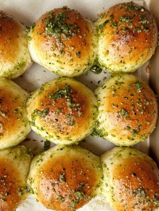 Close-up of golden brown pull-apart buns generously topped with green pesto and baked in a rectangular pan